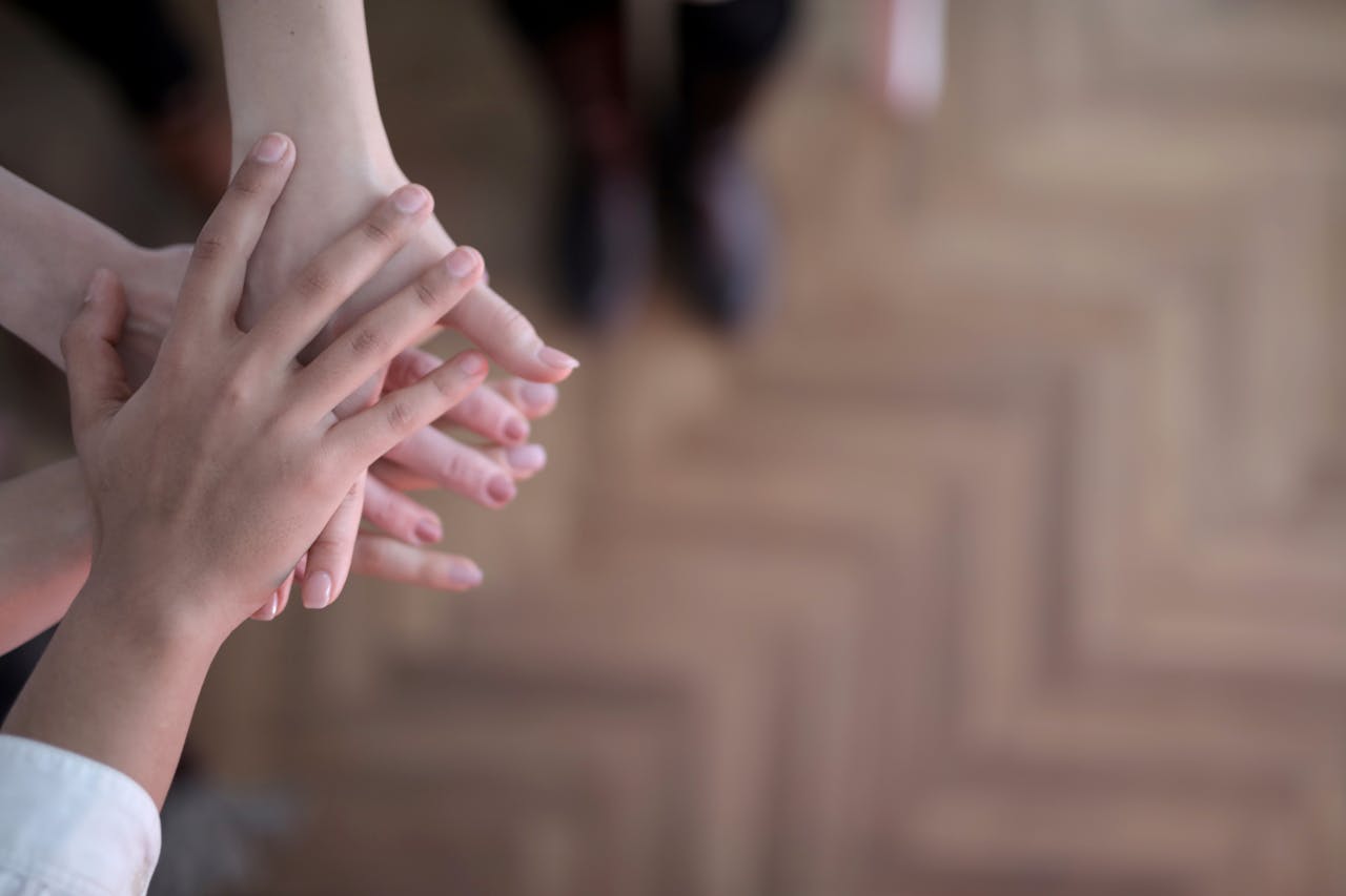 hero-img-02 Unrecognizable crop people holding hands together in teamwork and support above wooden brown floor