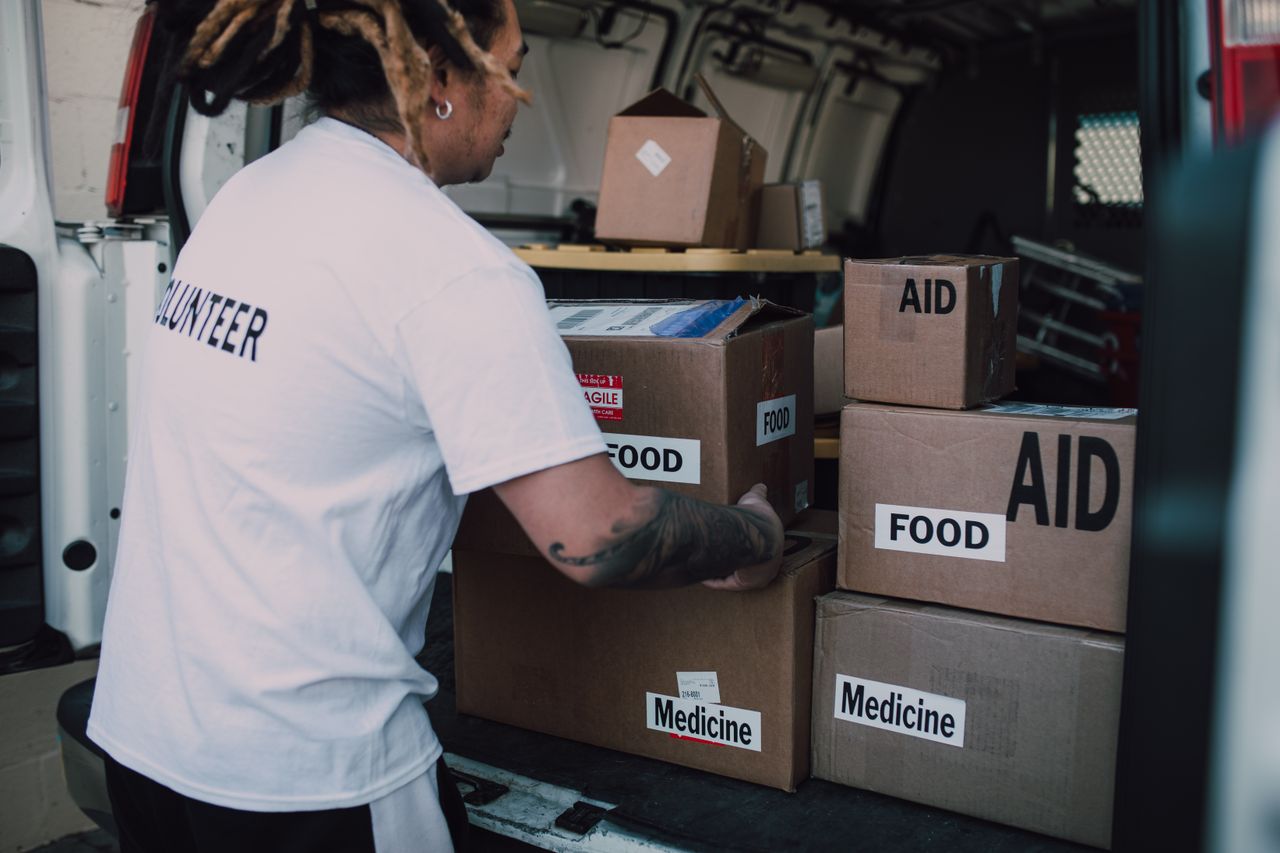 why-choose-us A volunteer organizes aid boxes containing food and medicine in a van for community service.