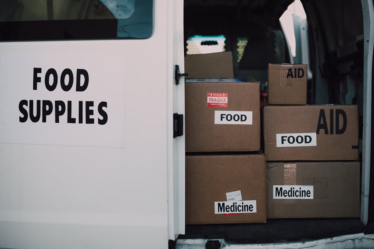 gallery-3 Stacked donation boxes labeled food and medicine in a delivery van for charity aid.