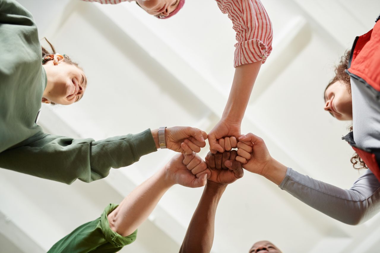 about-01 Four diverse team members join fists together, displaying unity and teamwork.
